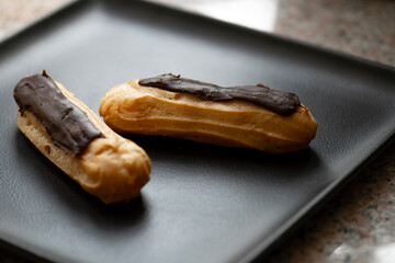Chocolate eclairs on a black plate .