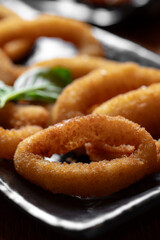 Fried onion rings on a black plate with basil leaves, selective focus