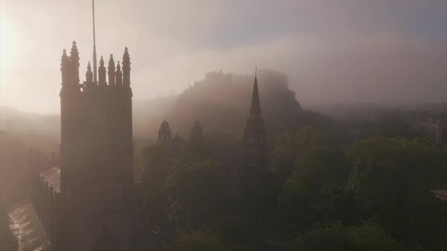 Aerial view of church with a tall steeple and castle in the background shrouded in a mystical fog, creating a scene of ethereal beauty, Edinburgh, United Kingdom.