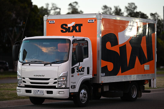 Orange Sixt hire truck, an Isuzu NNR 45-150, parked on the side of the road during the early evening