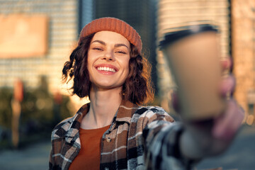 Woman smile coffee outdoor portrait beanie, candid lifestyle portrait of a young woman offering a takeaway cup in golden hour glow with authenticity, mindful living and emotional storytelling.