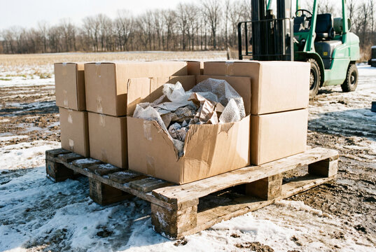Cardboard boxes with waste paper on wooden pallet near forklift in snowy field