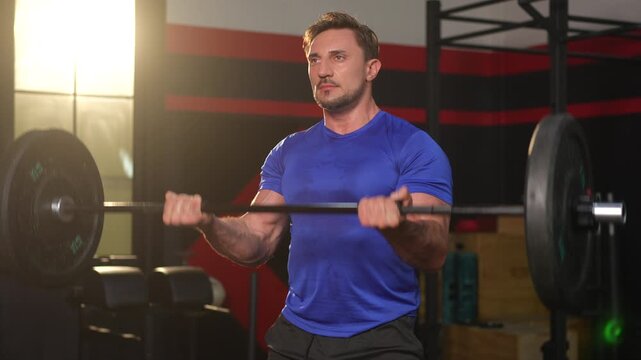 Muscular man blue shirt gym barbell weightlifting strength workout fitness training exercise focused muscular man gym lifting barbell for strength and fitness during intense bicep curl workout