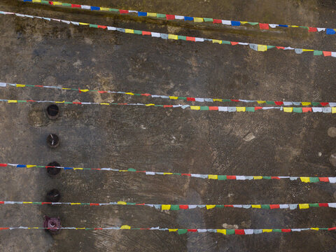 Aerial view of vibrant prayer flags stretch across the concrete, a tapestry of color against the muted gray, Bhutan.