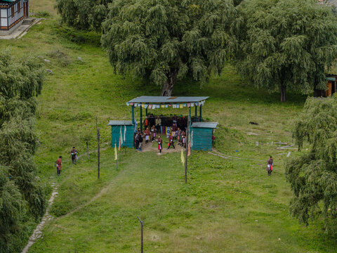 Aerial view of vibrant prayer flags fluttering above a gathering beneath a simple structure nestled in the verdant hills of the countryside, Thimphu, Bhutan.