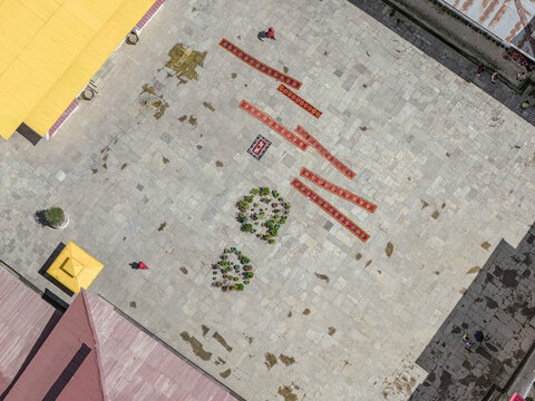 Aerial view of the courtyard of Gangtey Monastery, adorned with red carpets and greenery, contrasting against the gray stone, Gangtey Monastery, Phobjikha valley, Bhutan.