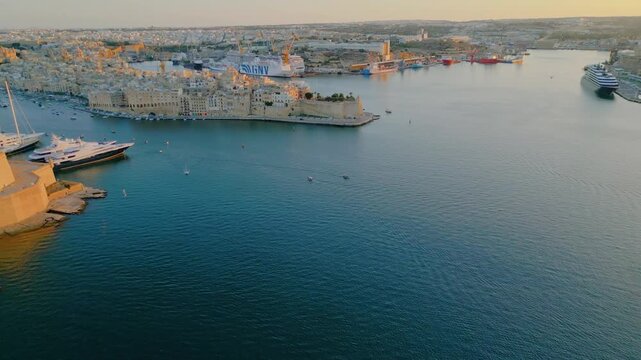 Epic Malta Valletta Grand Harbour sunset aerial panorama. 
Cinematic drone descending panning flight of historic Fort St Angelo, 
luxury yachts marina, medieval limestone bastions and sea water.
