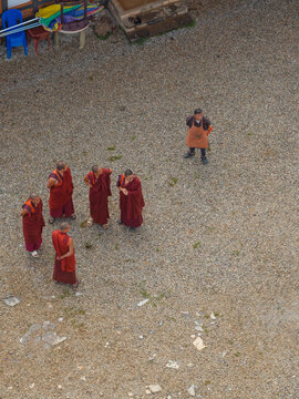 Aerial view of monks in vibrant red robes gathered on a light-colored gravel courtyard, a stark contrast against the muted tones, Paro, Bhutan.