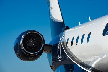 Close-up rear section of small business jets fuselage and top mounted rear turbofan engine. Clear blue sky fills the background.