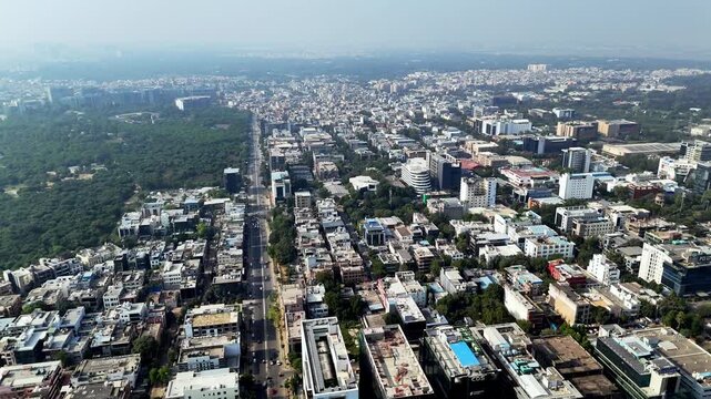 A sweeping or orbiting aerial (drone) shot capturing the modern, high-rise skyline of Gurugram, Haryana, India. The frame prominently features the glass office towers of the renowned DLF Cyber City