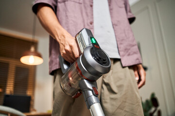 Fototapeta premium Man holding cordless vacuum cleaner, cleaning modern home interior, close up on hand and device, demonstrating household chores and contemporary cleaning technology