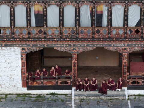 Karpo Lhakhang, Bhutan - 25 September 2025: Aerial view of monks in maroon robes gather on the ornately carved balconies of a traditional building, bathed in soft light.