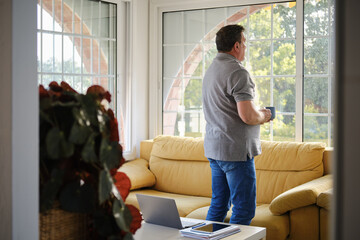 Mature man holding coffee mug looking out window