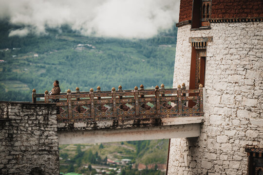 Paro, Bhutan - 17 September 2025: View of a solitary figure gazing out from a bridge at the National Museum, the stone walls contrasting with the distant soft mountains.