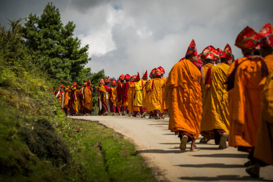 Nubding, Bhutan - 21 September 2025: View of monks in vibrant orange robes and elaborate red hats processing along a winding road in Phobjikha Valley.
