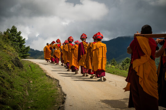Nubding, Bhutan - 21 September 2025: View of monks in vibrant saffron robes ascending the winding road, their procession a vivid contrast against the serene valley and towering mountains.