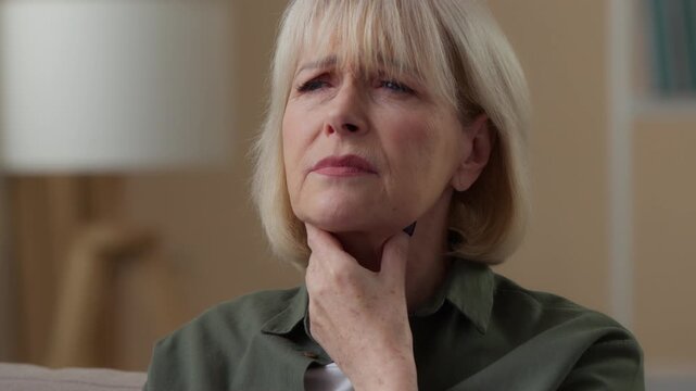 Old Caucasian woman feeling pain in throat at home holding neck retired sick female senior lady feel bad unhealthy suffering ache disease tonsillitis inflammation difficulty swallowing health problem