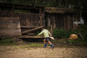 Ogyencholing, Bhutan - 23 September 2025: View of a child in blue boots sprints across the muddy ground, past weathered wooden structures, a glimpse of rural life.