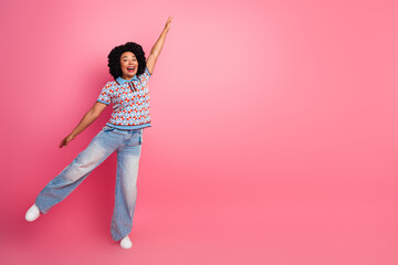 Happy young woman jumping with joy wearing a patterned shirt and jeans against a pink background...