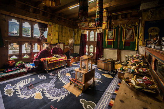 Ogyencholing, Bhutan - 23 September 2025: View of two monks inside a traditional room with ornate dragon carpet, wooden furniture, and vibrant religious tapestries.