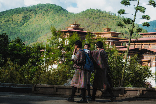 Punakha, Bhutan - 19 September 2025: View of young students clad in traditional attire walking past the majestic Punakha Dzong, set against a backdrop of lush green mountains, under a serene sky.