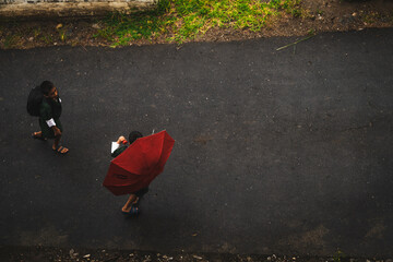 Punakha, Bhutan - 19 September 2025: View of two individuals walking along a dark asphalt road, one shielded by a vibrant red umbrella against the elements.