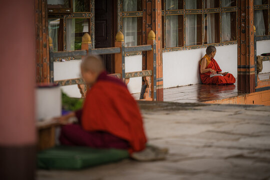 Walakha, Bhutan - 19 September 2025: View of monks in vibrant red robes sitting in quiet contemplation near Sangchhen Dorji Lhuendrup Lhakhang Nunnery.