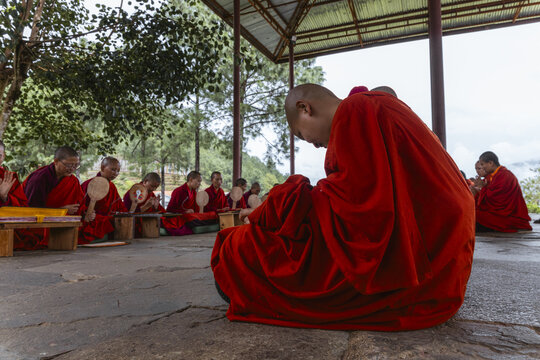 Punakha, Bhutan - 19 September 2025: View of crimson-robed nuns in Wolakha Nunnery, heads bowed in prayer, their fans and books a pale contrast to the vivid red under a simple roof.