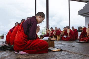 Punakha, Bhutan - 19 September 2025: View of crimson-robed nuns, heads bowed in prayer, a sea of serenity against the backdrop of Wolakha Nunnery's stark white walls and misty mountains.