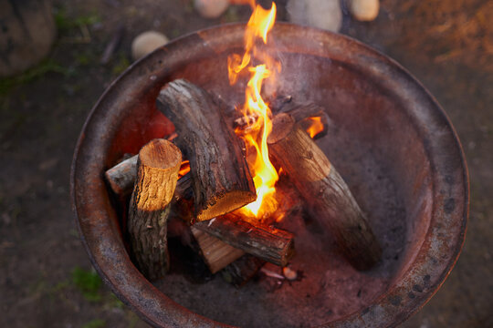 Outdoor, bonfire and wood with flames in grill stand, smoke and embers burning for barbecue preparation. High angle, heat source and glowing log with sparks in backyard, camping and weekend activity