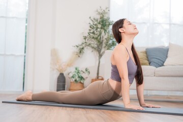 Young woman practices yoga at home in morning light, focusing on her breath in a cobra pose on a mat