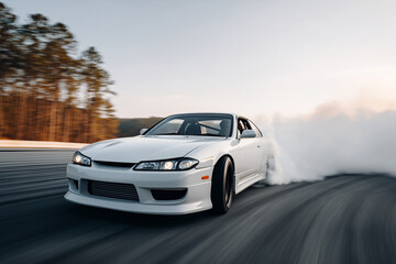 Obraz premium White sports car drifts at high speed on a racetrack with tire smoke and dynamic motion.