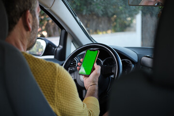 Person holding smartphone with green screen while driving car. unrecognizable person
