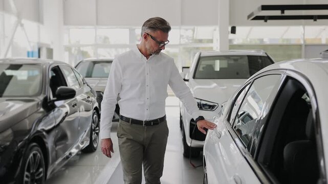 Smiling happy rich man customer male buyer client wears white shirt chooses auto wants to buy new automobile walk go in car showroom vehicle salon dealership store motor show indoor. Sales concept