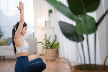 Woman stretches arms in a bright indoor space while sitting on a mat in the morning