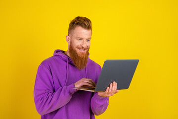 Young man in purple hoodie uses laptop against bold yellow background displaying casual fashion and stylish lifestyle for advertising and shopping campaigns