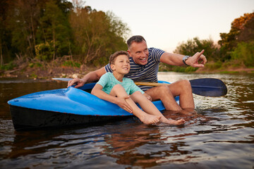 Obraz premium Happy father, son or sightseeing with canoe in lake for travel or outdoor journey in nature. Child, kid or dad pointing with view, kayak or sunset on water or river for holiday adventure or bonding
