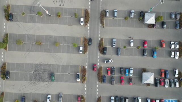 Aerial view of busy parking lot near shopping center, showcasing various parked vehicles, camera pans across scene highlighting parking dynamics and space utilization