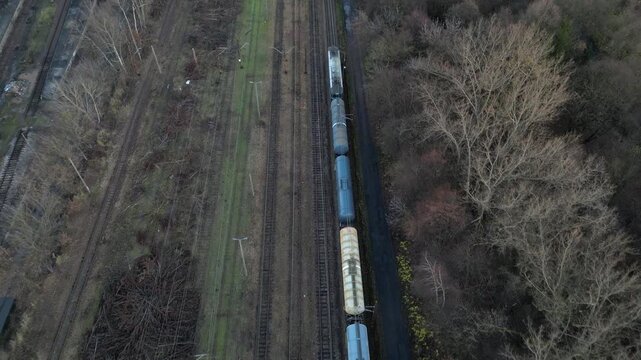 Aerial perspective captures a winding train track lined with freight cars, surrounded by vibrant greenery and textured terrain, as the camera pans to enhance the scene's visual richness