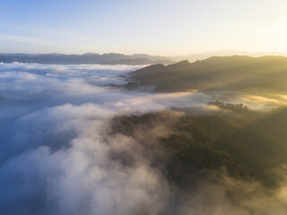 Fototapeta premium Serene aerial view of mountain landscape covered in sea of fog at sunrise. Beautiful golden light illuminates morning sky and misty clouds over natural scenery