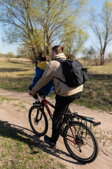 Father rides his little son on the handlebars of a bicycle in a meadow