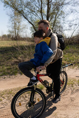 Father rides his little son on the handlebars of a bicycle in a meadow