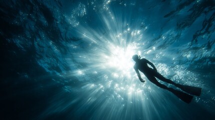 A silhouette of a person swims upwards in deep blue water, sunlight streaming from above, creating a radiant effect