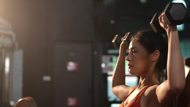 Health conscious Asian woman lifting weights at the gym to strengthen arm muscles and improve fitness. Ideal for concepts of strength training, healthy lifestyle, women wellness, and self care.