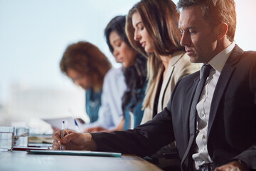 Obraz premium Businessman, writing and team at office meeting with documents, audit or financial review at company. Person, notes and compliance paperwork with group, staff or collaboration at accounting agency