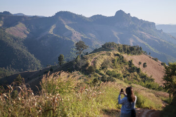 Peaceful female traveler taking photo with smartphone, enjoying scenic mountain view. beautiful landscape during sunny day of hiking and outdoor adventure