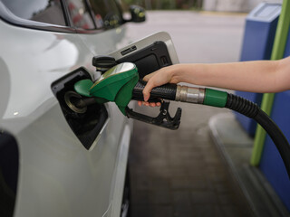 Close up of person refueling a car at a gas station using a green fuel nozzle. Concept of transportation, energy, travel readiness, routine, technology, and modern lifestyle.