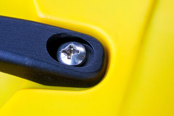 Macro detail close up of shiny metal screw fastening black plastic part to bright yellow surface....