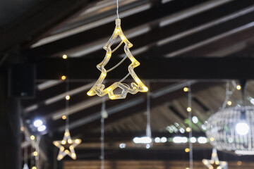 Festive hanging Christmas tree light ornament glowing with warm illumination. This cheerful holiday decoration creates cozy atmosphere with beautiful bokeh lights in background