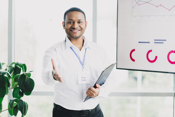 Confident young businessman in bright office presents clipboard open hand charts on large screen leadership and success in a modern corporate setting